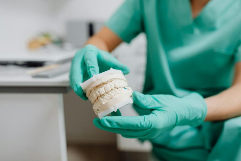 A close-up of hands in latex gloves holding a dental cast in a dental office.