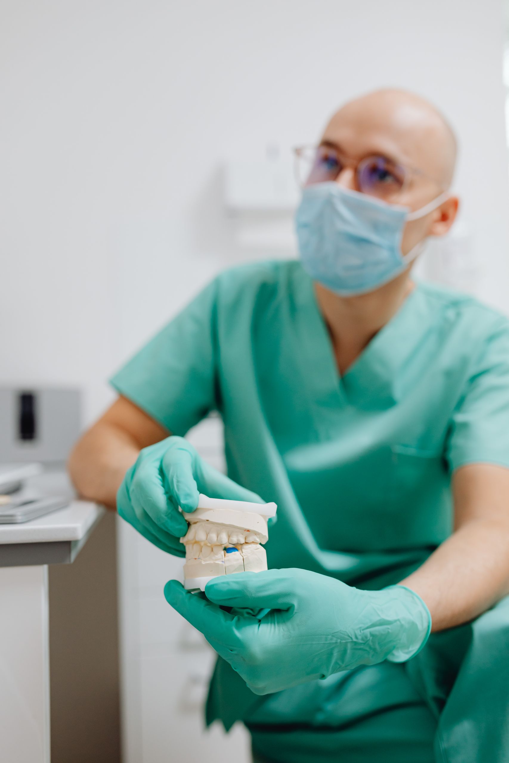 Dentist in surgical scrubs holding and demonstrating a dental model.